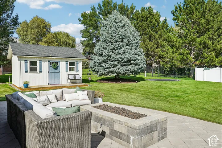 Spacious backyard featuring a paver patio with a built-in fire pit, a dedicated storage shed, and mature trees