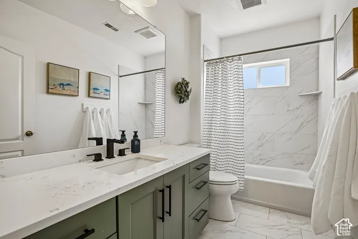 White tile flooring, single vanity with light green cabinetry, white countertop, rectangular undermount sink, and a shower/tub combination with white tile surround