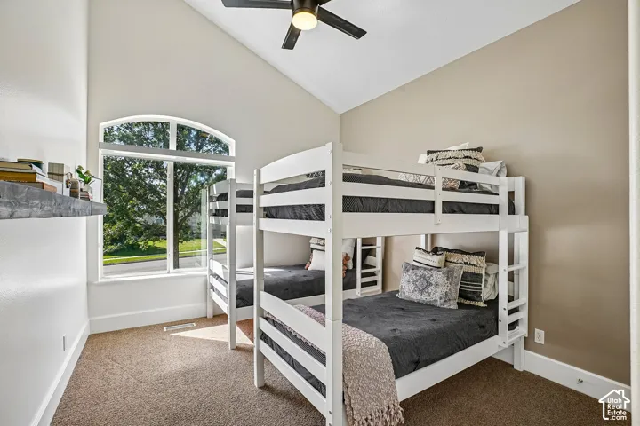 Vaulted ceiling, arched window, wall-to-wall carpeting, and a ceiling fan