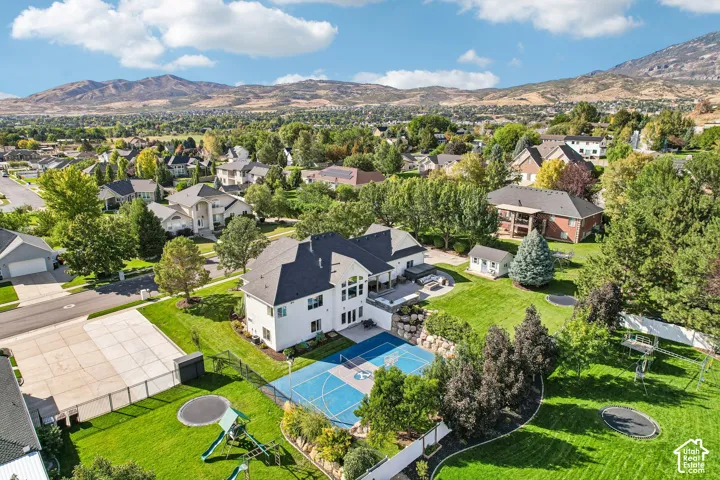 Expansive rear yard featuring a sports court, terraced landscaping, mature trees, and mountain scenery