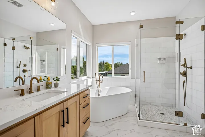Freestanding soaking tub, walk-in shower with clear glass enclosure, dual vanity with undermount sink, ample natural light, and tile flooring