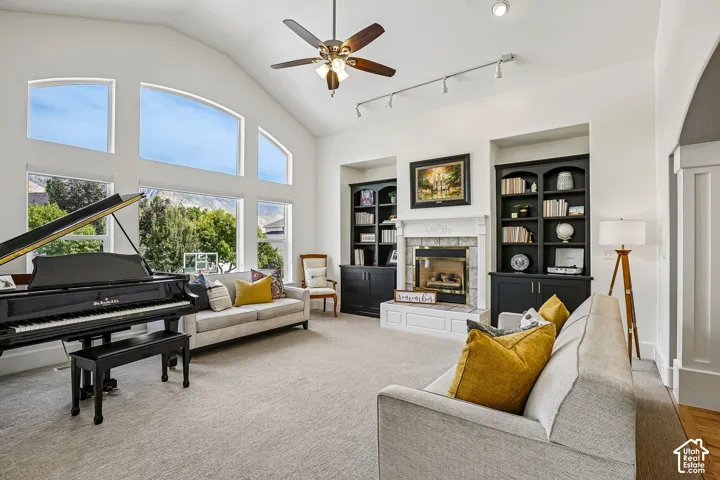 Vaulted ceilings, large arched windows, built-in shelving, fireplace with decorative mantel, and a ceiling fan with integrated lighting