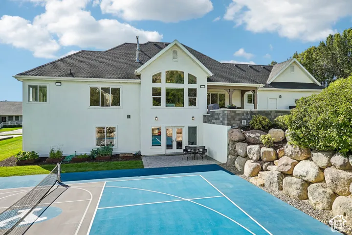 Spacious exterior featuring a multi-sport court, stone retaining wall, upper-level patio, ground-level patio, and large architectural windows