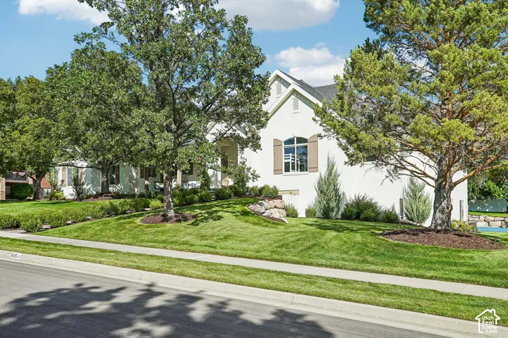 Stucco exterior with a peaked roofline, arched window with decorative shutters, mature trees, and landscaped grounds