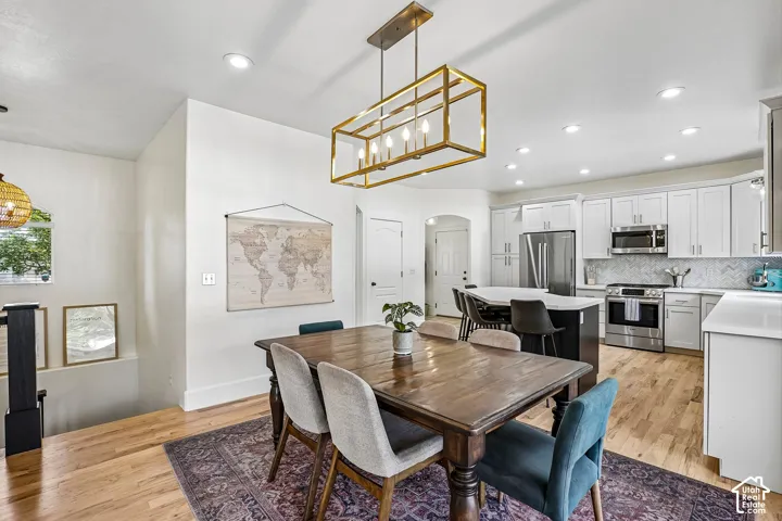 Open-concept kitchen and dining area featuring wood-finish flooring, white cabinetry, stainless steel appliances, and a central island with bar seating