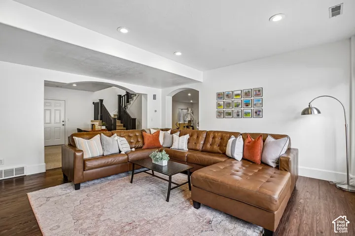 Wood-finish flooring, recessed ceiling lighting, arched doorways, and a dark wood staircase with painted risers