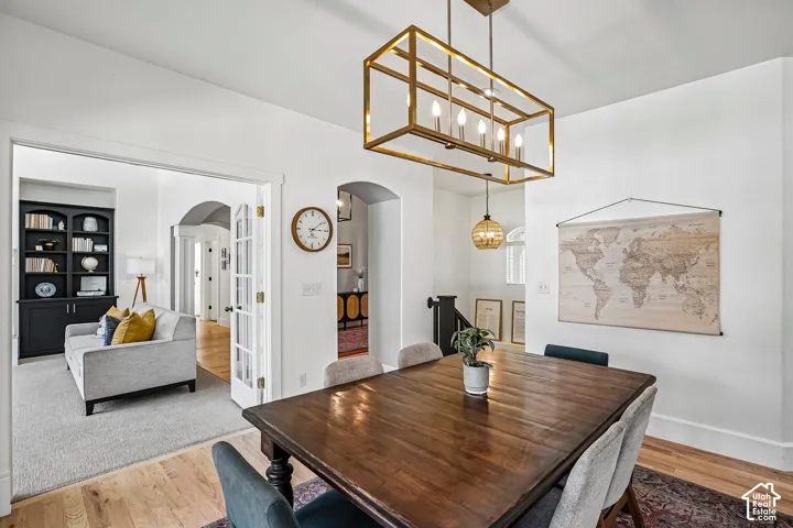 Spacious dining area with light wood-finish flooring, a rectangular brass chandelier, and an arched doorway