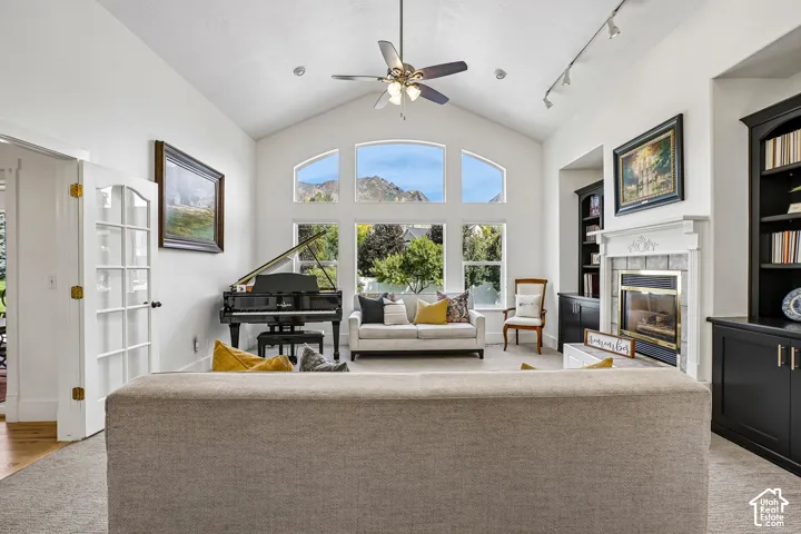 Vaulted ceiling with a ceiling fan, arched transom windows, and a fireplace with a decorative mantel and stone surround
