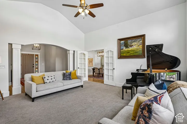 Vaulted ceiling with a ceiling fan, carpeted flooring, French doors, and an arched entryway with decorative columns