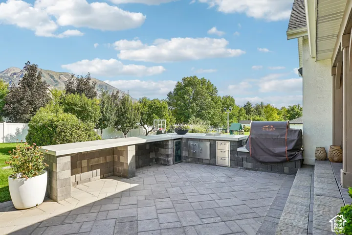 Paver patio featuring a built-in outdoor kitchen with stainless steel appliances, stone-look cabinetry, and an extended countertop