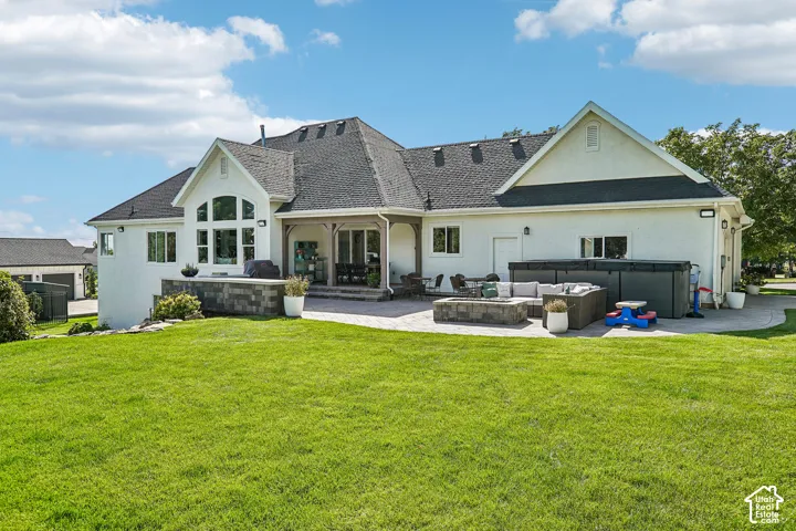 Expansive lawn with a stone paver patio, covered outdoor living area, and built-in fire pit