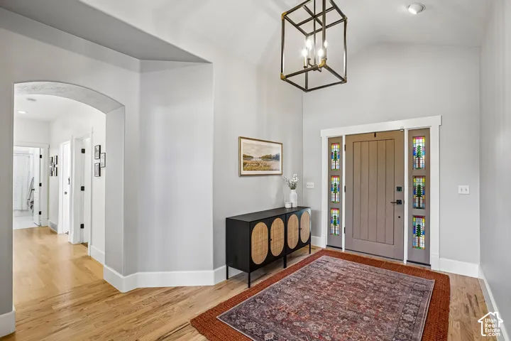 Vaulted entry featuring wood-finish flooring, an arched doorway, and a modern geometric chandelier