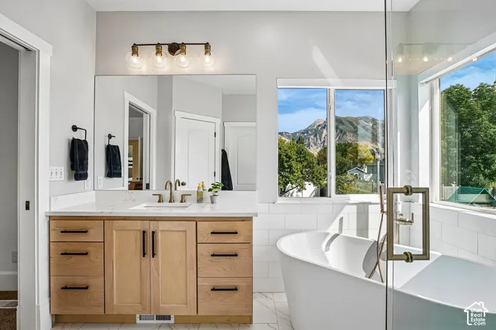 Freestanding soaking tub, wood-finish vanity with an integrated sink, quartz countertop, and glass-enclosed shower