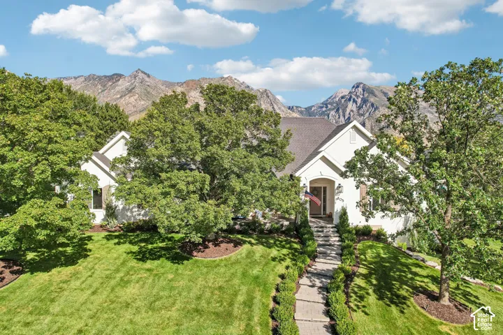Stucco exterior with a peaked roofline, a stone walkway, and established landscaping, framed by mountain scenery