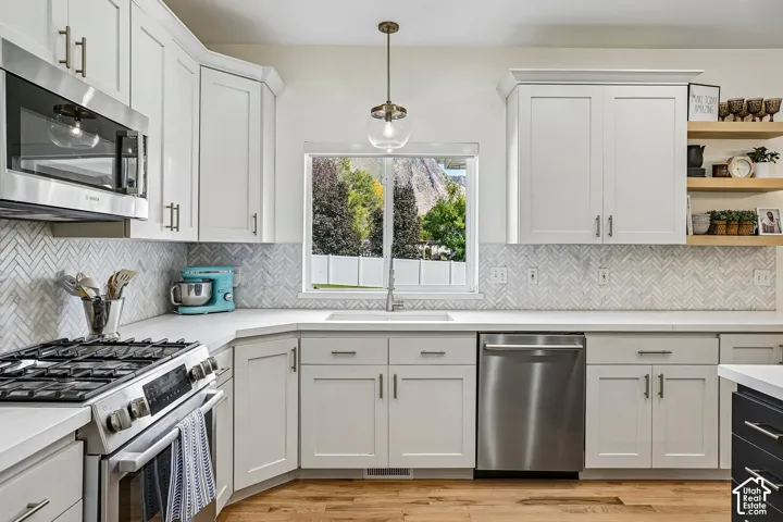 White shaker cabinetry with modern hardware, stainless steel appliances, herringbone tile backsplash, light-toned countertops, and wood-finish flooring