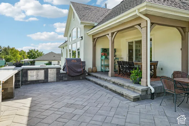 Expansive paver patio with a built-in outdoor kitchen, featuring a covered dining area and a stucco exterior