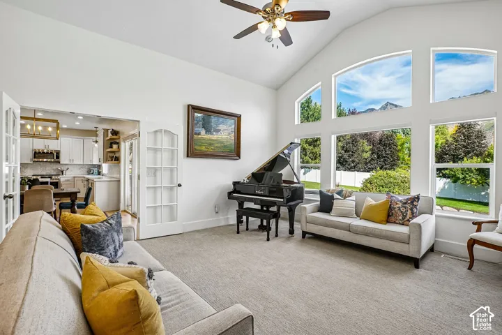 Vaulted ceiling with a ceiling fan, expansive windows, carpeted flooring, and French doors