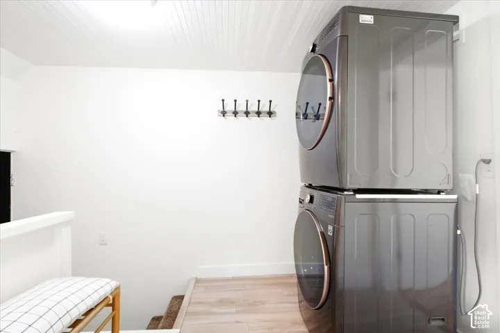 Stackable washer and dryer, wood-finish flooring, white paneled ceiling, and wall-mounted coat rack