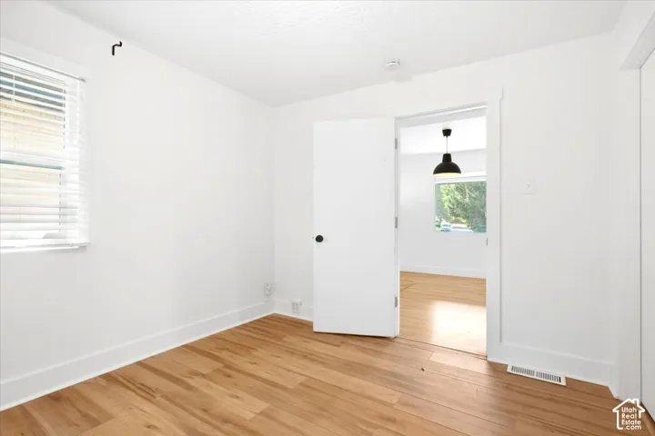 Wood-finish flooring with white trim, a single window with blinds, and white painted walls