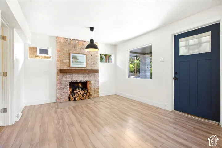 Exposed brick fireplace with a wood-finish mantel, wood-finish flooring, and white painted walls