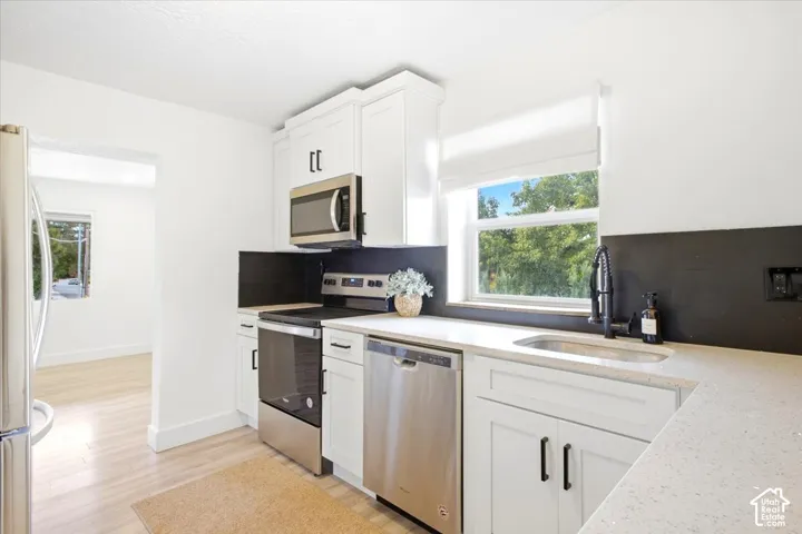 Kitchen featuring white shaker cabinetry, stainless steel appliances, light-toned countertops, and a matte black faucet