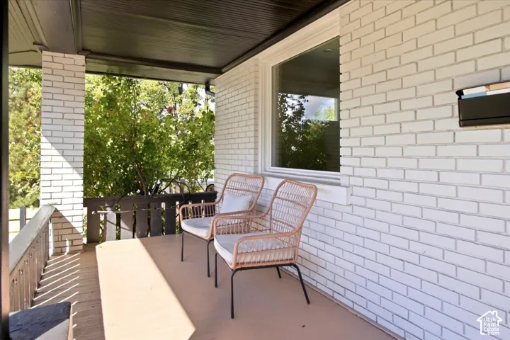 Covered front porch featuring white brick facade, dark wood-tone railings, and a large window with white trim