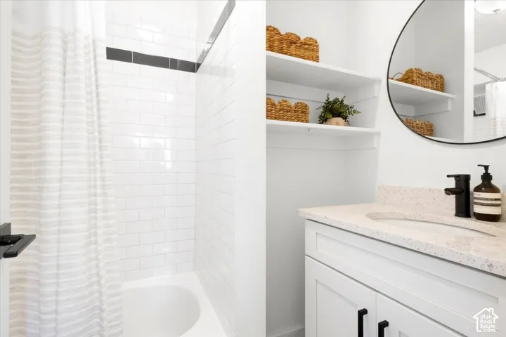White subway tile bath surround with a dark accent band, built-in shelving, white vanity with black hardware, and a circular wall-mounted mirror