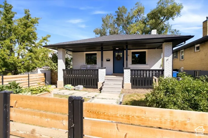 Brick exterior with a covered front porch featuring dark railings, a dark roof, and a visible front door