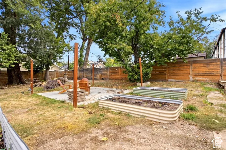 Expansive backyard featuring a concrete patio, wood fencing, and two raised garden beds