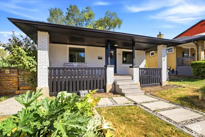 White brick exterior featuring a covered porch, black railing, concrete steps, and a paver pathway