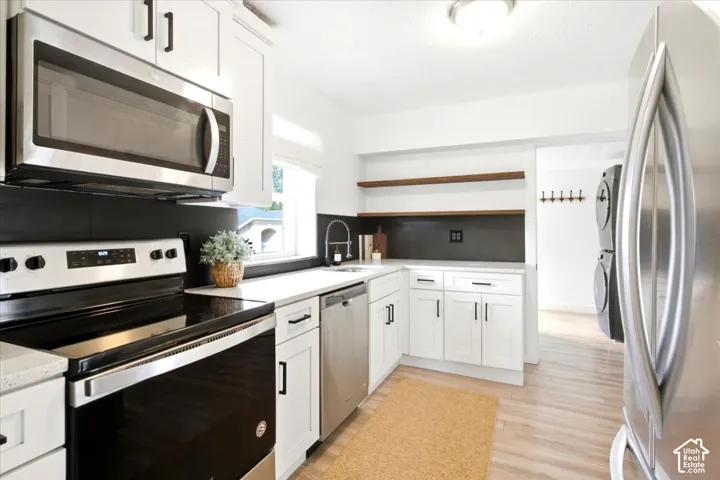 White shaker cabinetry, stainless steel appliances, light wood-finish flooring, and open shelving