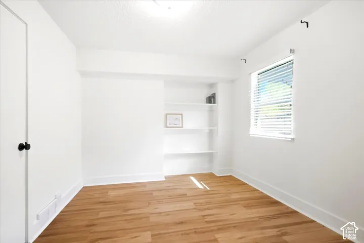 Wood-finish flooring with white baseboards, built-in shelving, and a window with blinds