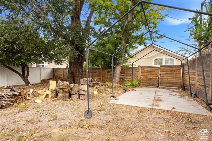 Expansive backyard featuring mature trees, a concrete pad, a metal frame structure, and wood privacy fencing