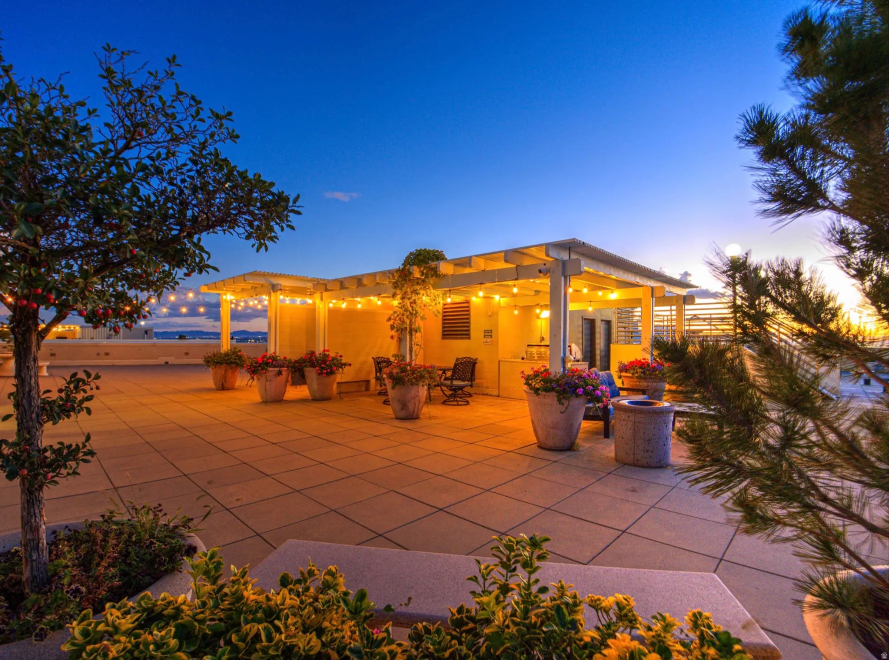 Expansive rooftop patio featuring a covered pergola, string lighting, and extensive hardscaping