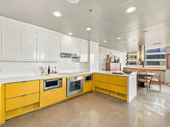 Contemporary kitchen featuring sleek white upper cabinetry, vibrant yellow lower cabinetry, integrated stainless steel appliances, white countertops, and recessed lighting