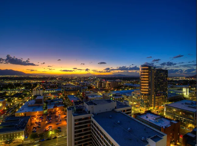 Panoramic cityscape with distant mountains, illuminated buildings, and a vibrant sunset horizon