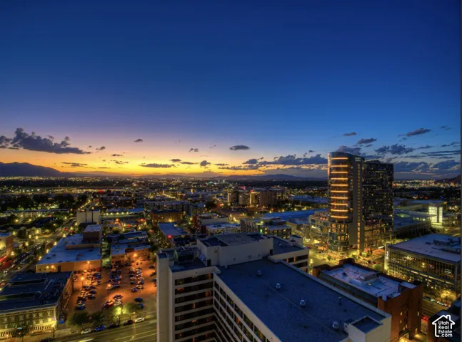 Panoramic cityscape with distant mountains, illuminated buildings, and a vibrant sunset horizon