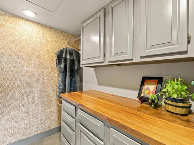 Recessed lighting illuminates a patterned wall, complemented by light gray cabinetry with a wood-finish countertop
