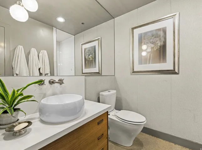 White vessel sink with wall-mounted faucet, wood-finish vanity with drawer storage, and a white toilet