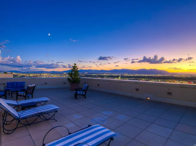 Expansive rooftop patio with a tiled surface, low perimeter wall, and distant city lights