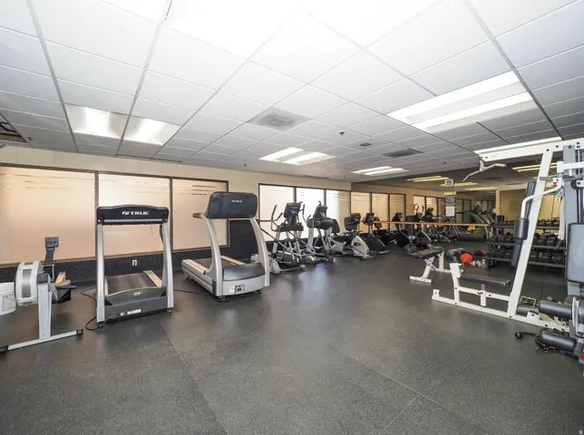 Fitness room with resilient flooring, multiple cardio machines, weight training equipment, and acoustic ceiling tiles