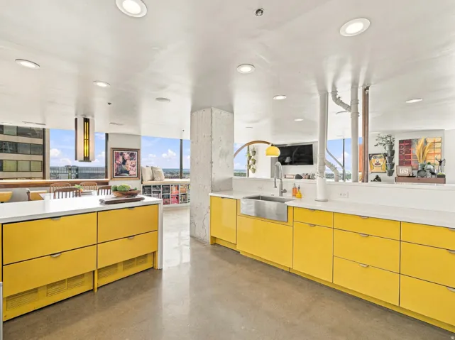 Modern kitchen featuring bright yellow cabinetry, white countertops, and a stainless steel farmhouse sink