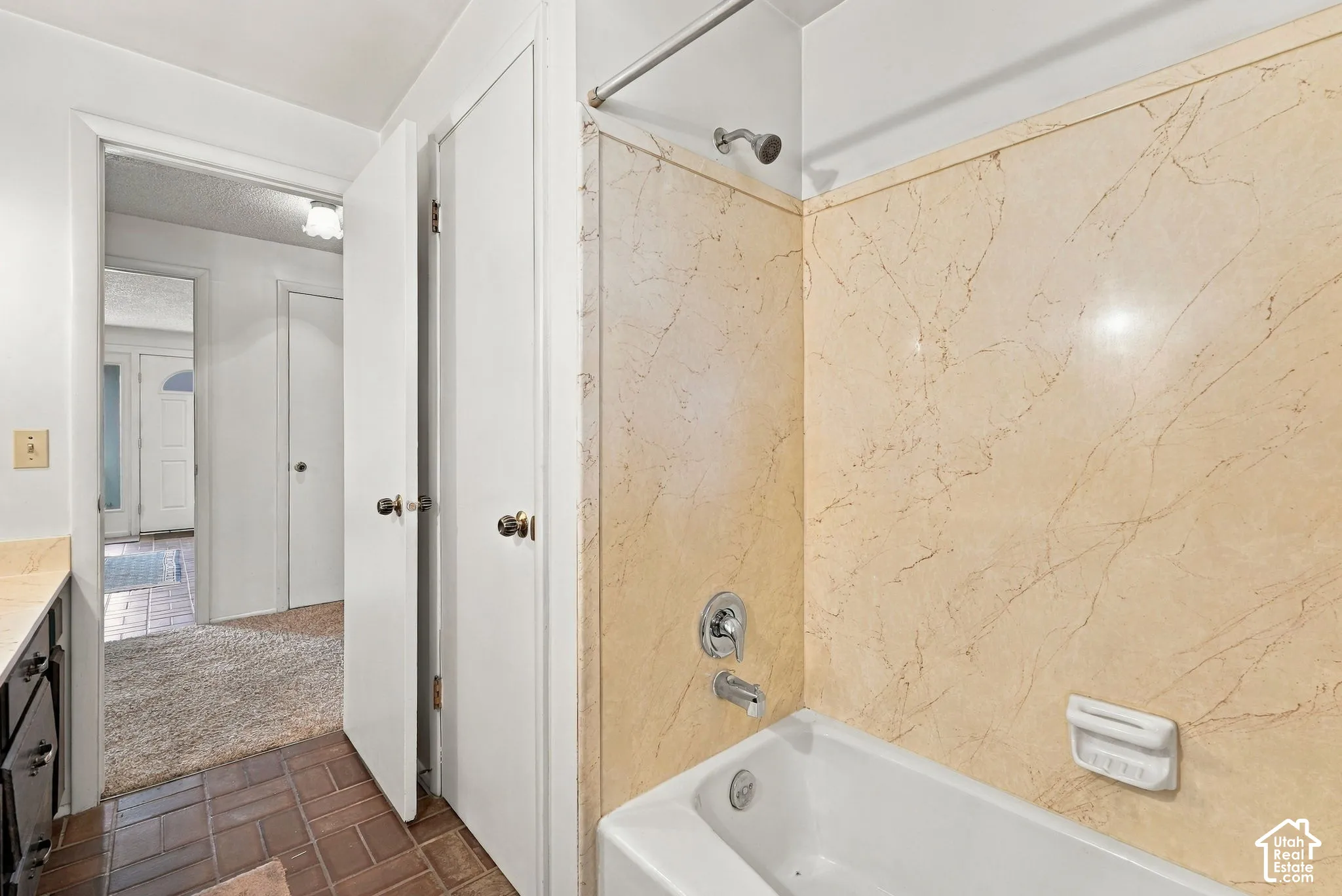 Bathtub with a chrome shower fixture, light-toned wall paneling, and a soap dish