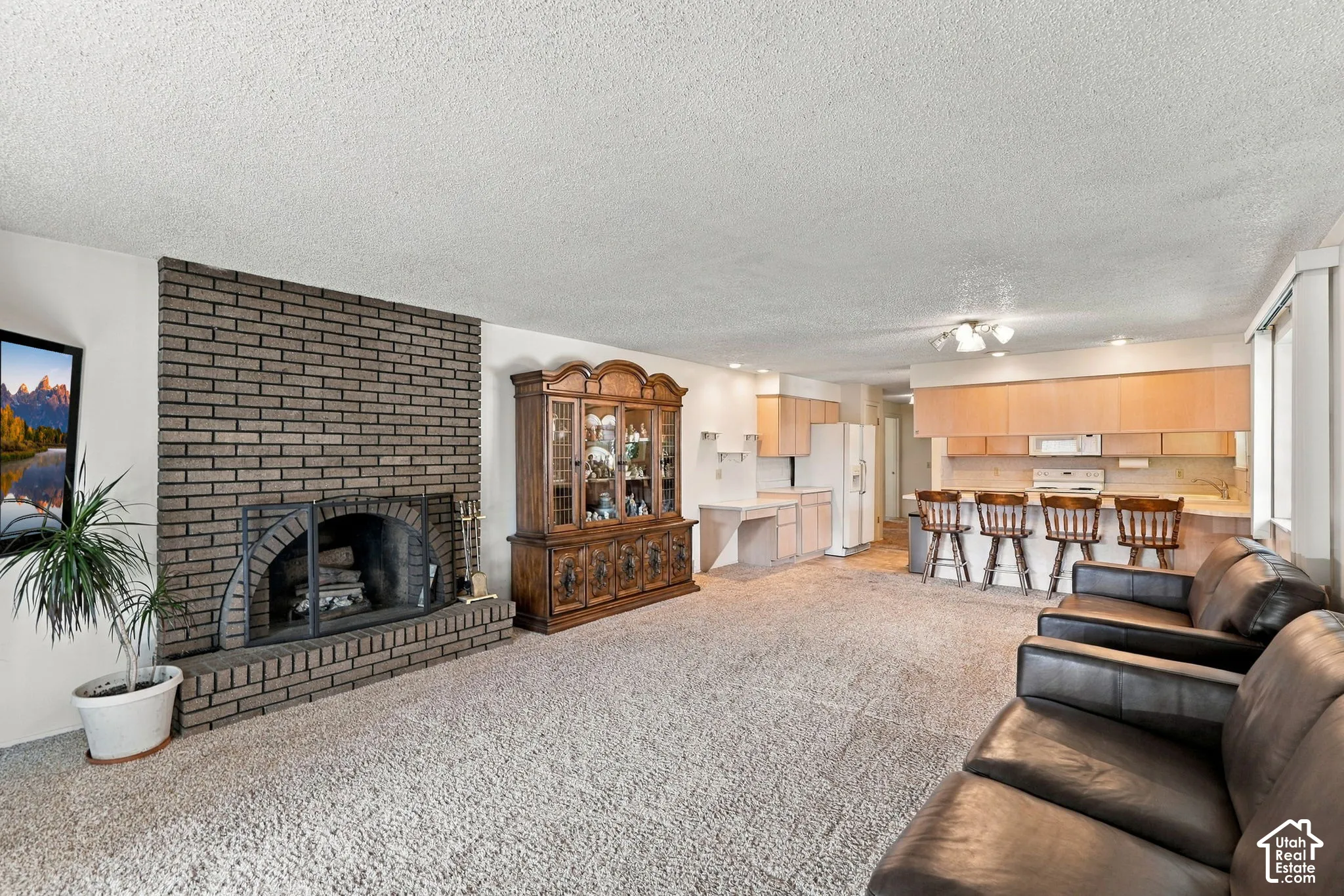 Spacious open-concept living area featuring a brick fireplace with wood-burning insert, neutral carpet flooring, and leather seating