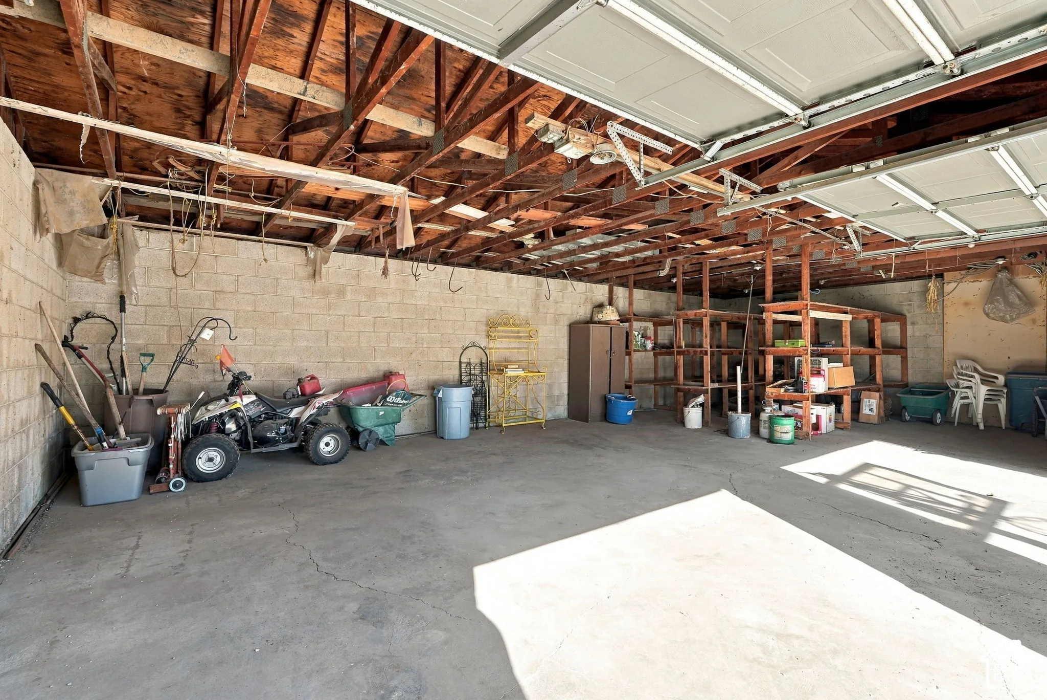 Open garage space with concrete flooring, exposed wood beam ceiling, and concrete block walls