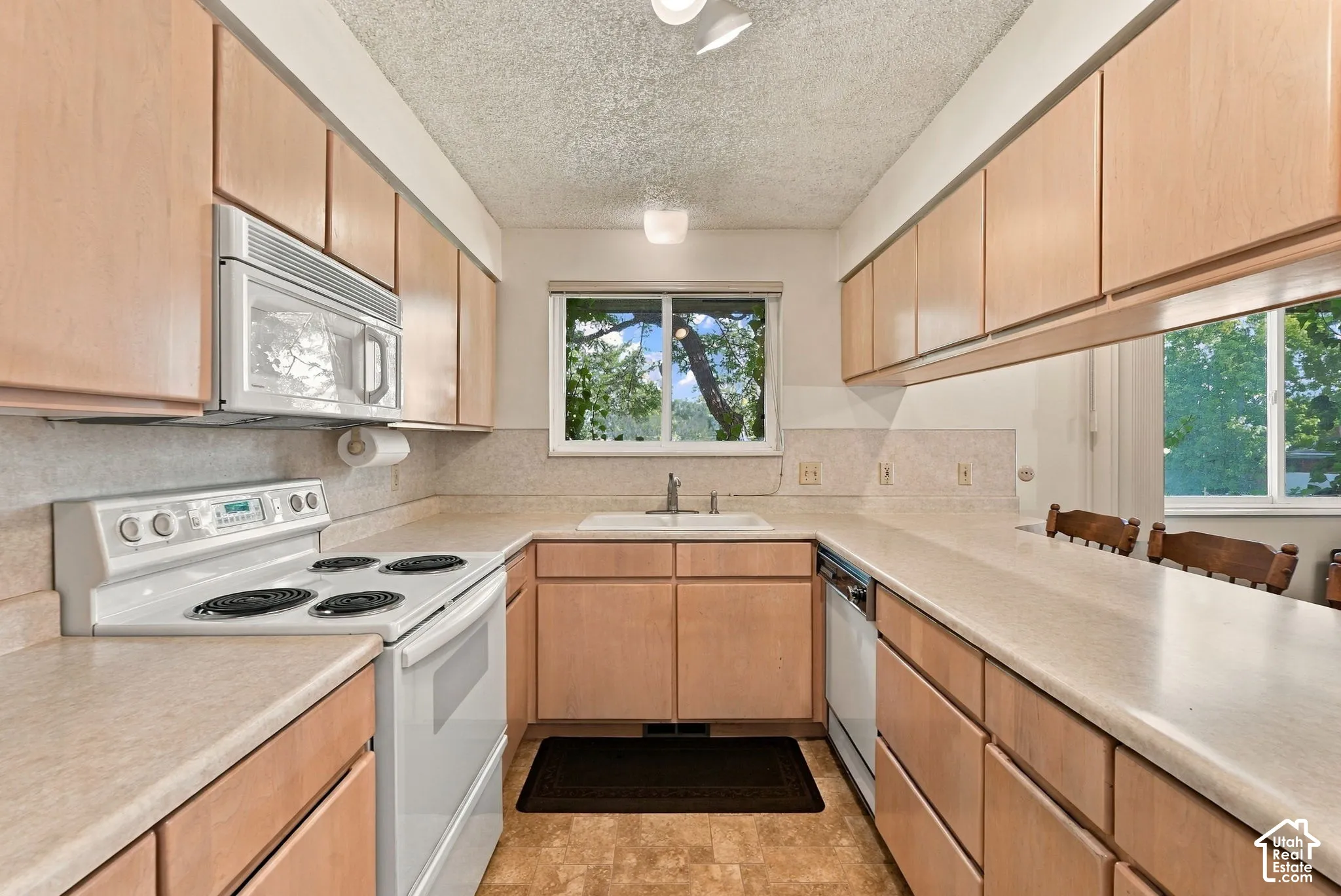 Galley kitchen featuring light wood-finish cabinetry, a white electric range, and a built-in microwave
