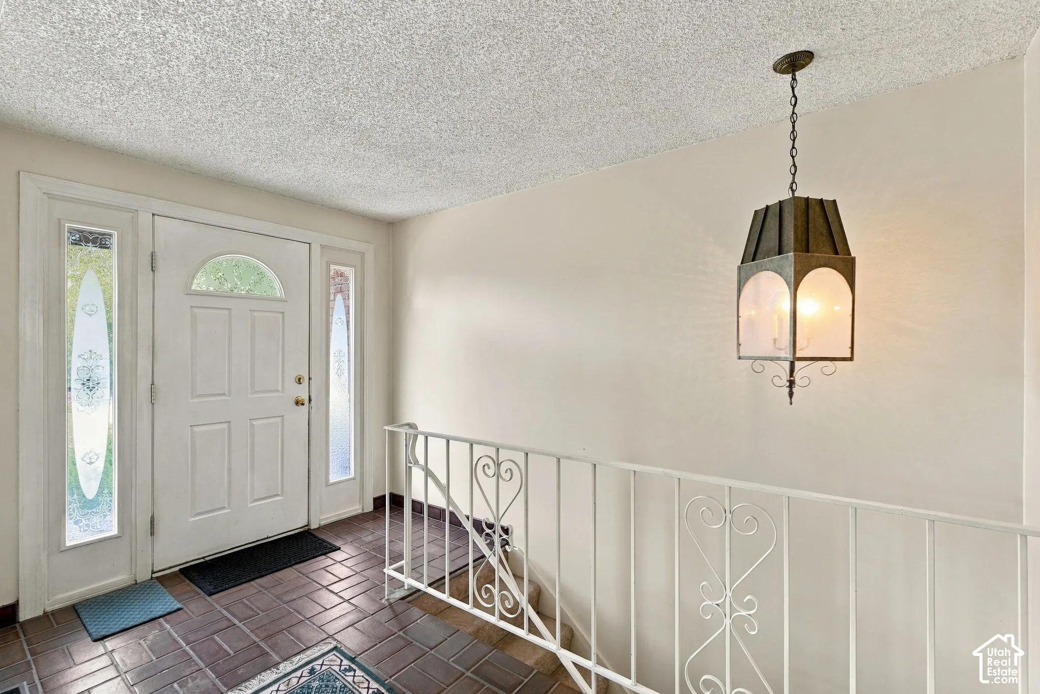 Entryway featuring a paneled door with an arched transom, sidelight windows, a decorative metal handrail, and a hanging pendant light fixture