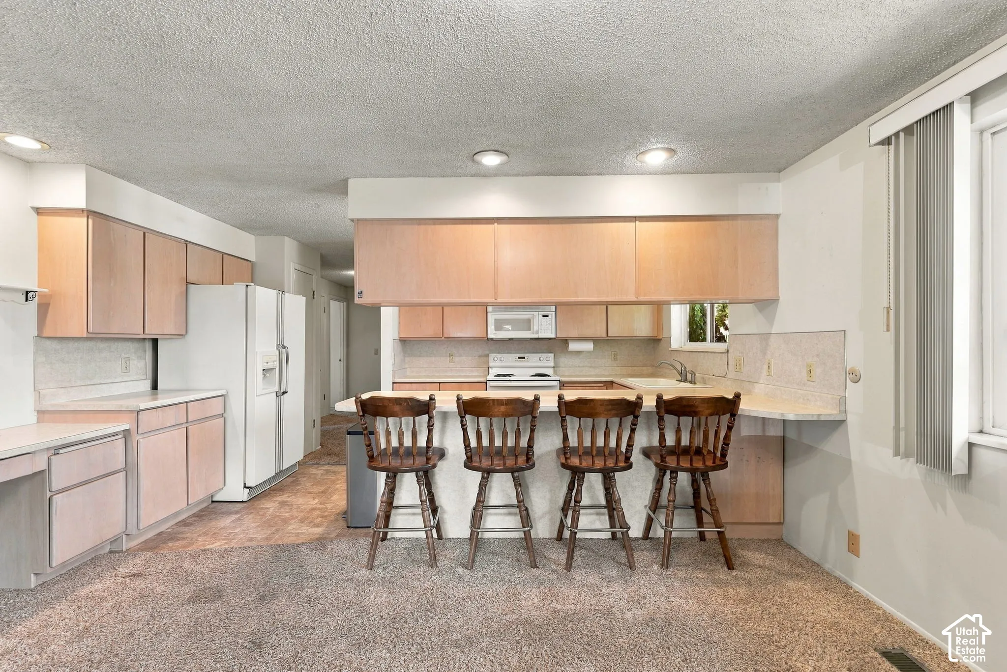 Open-concept kitchen featuring wood-finish cabinetry, built-in appliances, and a breakfast bar with stone-finish countertops