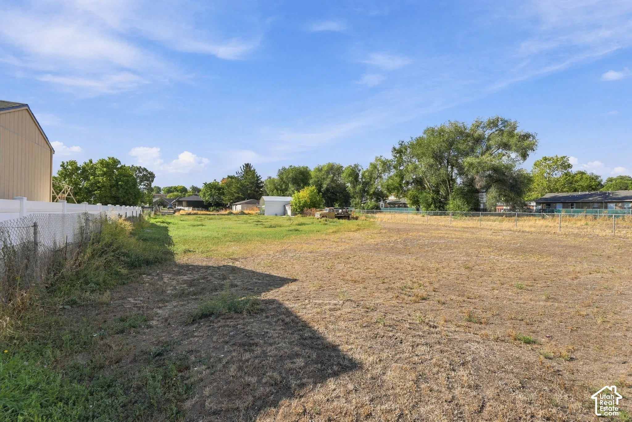 Expansive open lot featuring a white privacy fence and a chain link fence
