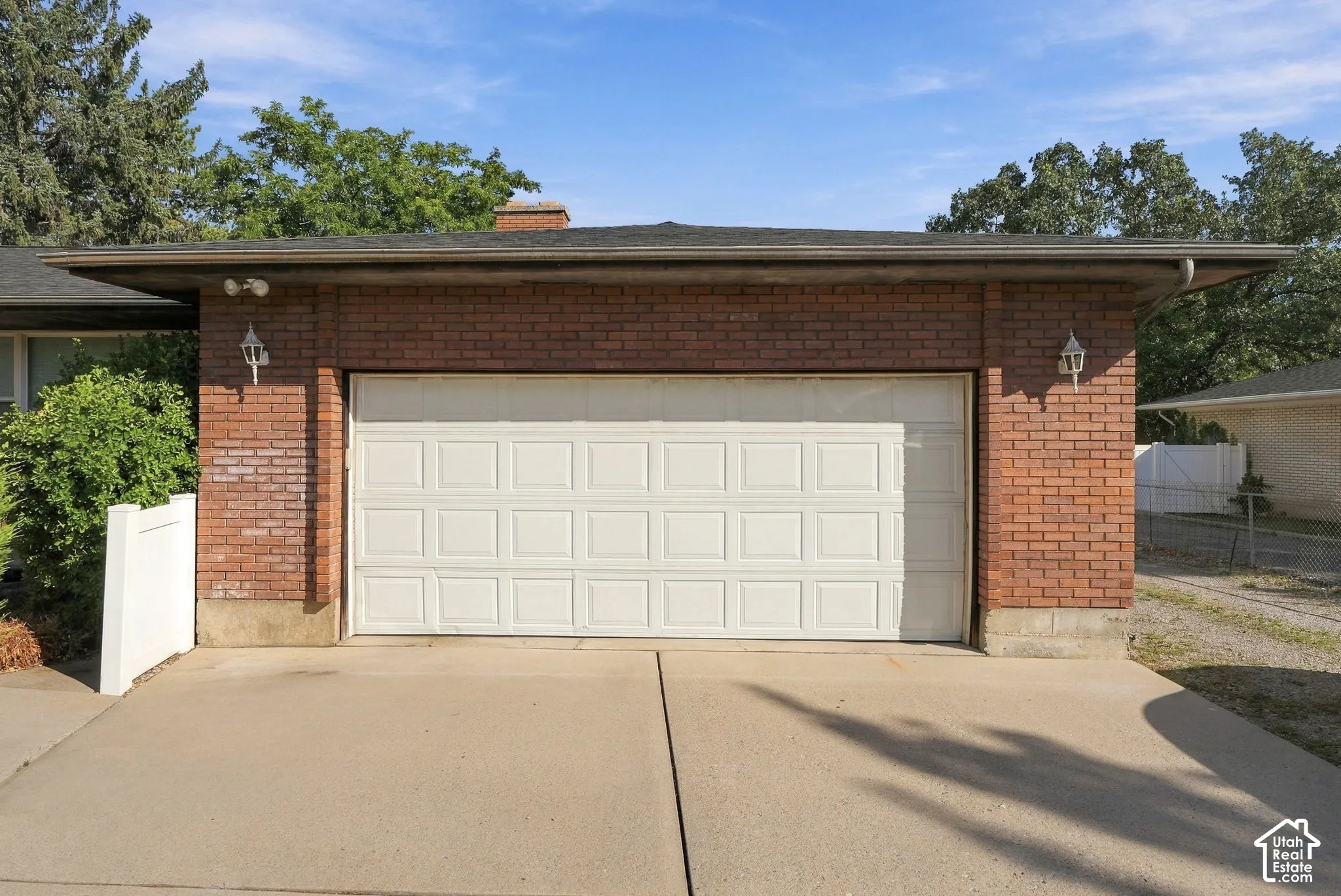 Brick exterior with a white panel garage door, complemented by two exterior sconce lights and a concrete driveway